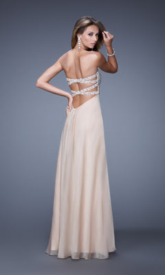 A woman wearing the La Femme Dress 20784, a floor-length, strapless chiffon gown with an embellished bust, sparkling strap details, and an open back, stands against a plain gray background.