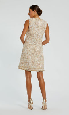 A woman faces away, modeling the Mac Duggal 20795 Semi-Formal Shift Dress with a beaded hemline and sleeveless design, paired with metallic high heels against a plain backdrop.