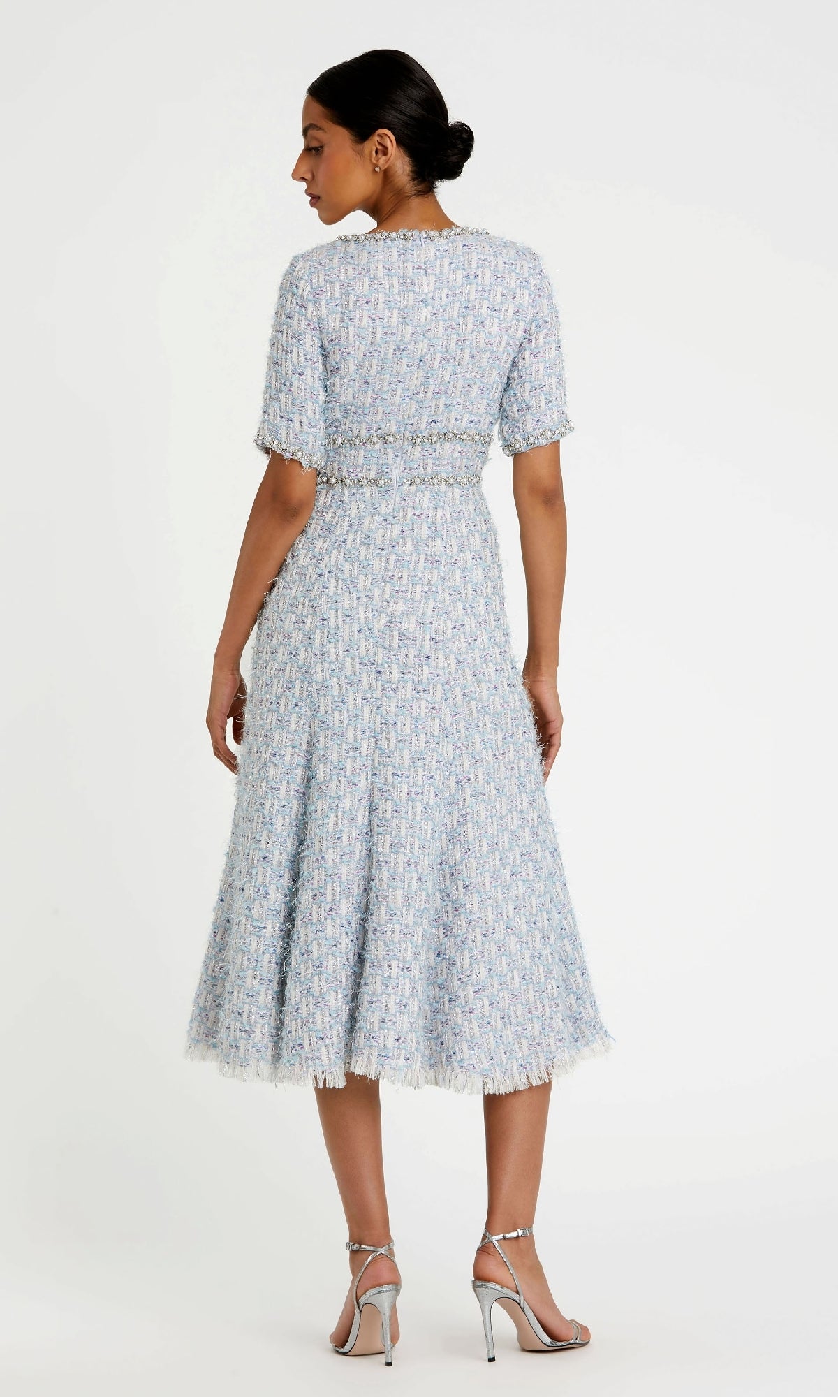 A woman faces away, wearing the Mac Duggal 20806— a light blue, tea-length textured cocktail dress with fringe hem and short sleeves—styled with silver heels; perfect as a chic short blue wedding guest dress.