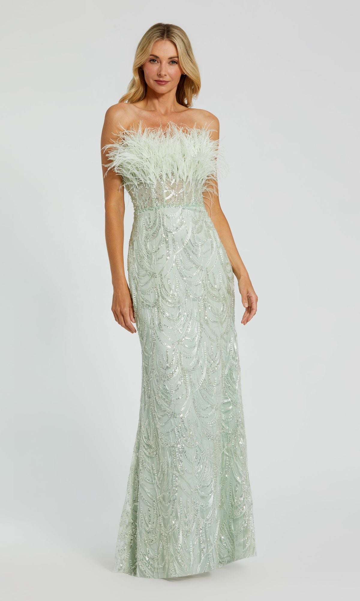 A woman wears the Mac Duggal 20890 Long Mint Sequin Prom Dress, a strapless gown with sequin patterns and a feather-trimmed neckline, standing against a plain background.