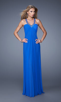 A woman poses against a gray background, hands on hips, wearing the La Femme Dress 20903—a floor-length royal blue gown with embellished straps.