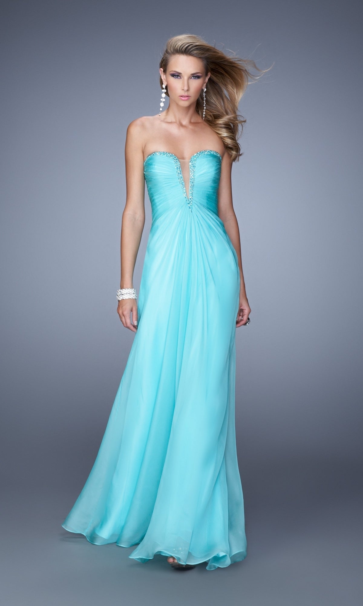 A woman poses against a gray background in the La Femme Plunging-Sweetheart Prom Dress 20930, a strapless, floor-length aqua chiffon gown with a deep neckline, paired with earrings and bracelets.