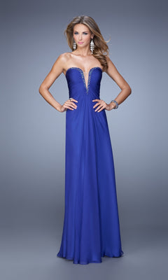A woman wearing the La Femme Plunging-Sweetheart Prom Dress 20930—a strapless, floor-length royal blue gown with a deep V-neckline and rhinestone accents—stands against a gray background.