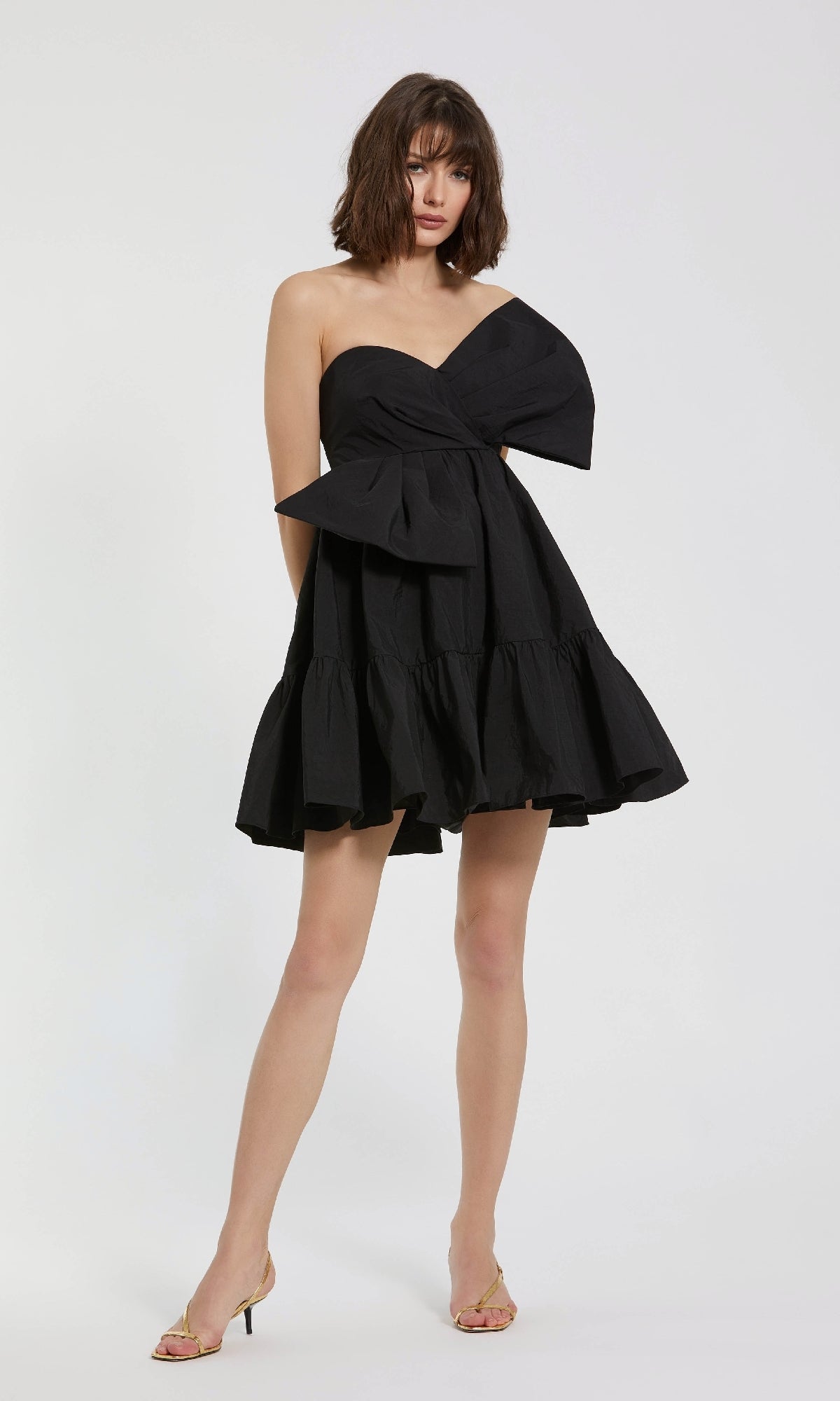 A woman models the Strapless Short Bow Party Dress: Mac Duggal 20937, featuring a tiered skirt and large bow, standing against a plain white background.