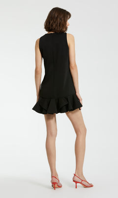 A woman faces away, wearing the Mac Duggal 20957 black cocktail party dress with a ruffled crepe hem and red strappy heels, set against a plain white background.