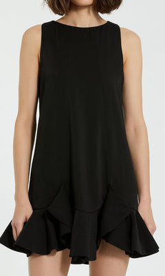 A woman models the Mac Duggal 20957, a sleeveless black cocktail party dress with a flounced hem in elegant crepe, standing before a plain light background.