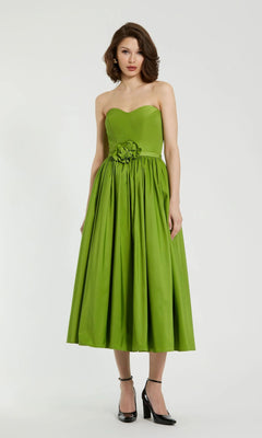 Woman in the Mac Duggal 21023 midi strapless semi-formal dress, green with a fitted bodice, flared tea-length skirt, and waist floral detail—styled with black heels—a chic pick for any semi-formal event.
