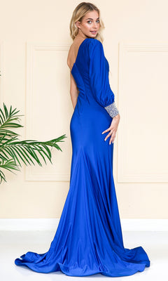 A woman wearing the Embellished-Cuff One-Sleeve Long Prom Dress 2102 in royal blue stands sideways, looking over her shoulder in a minimalist room with beige walls and a green plant.