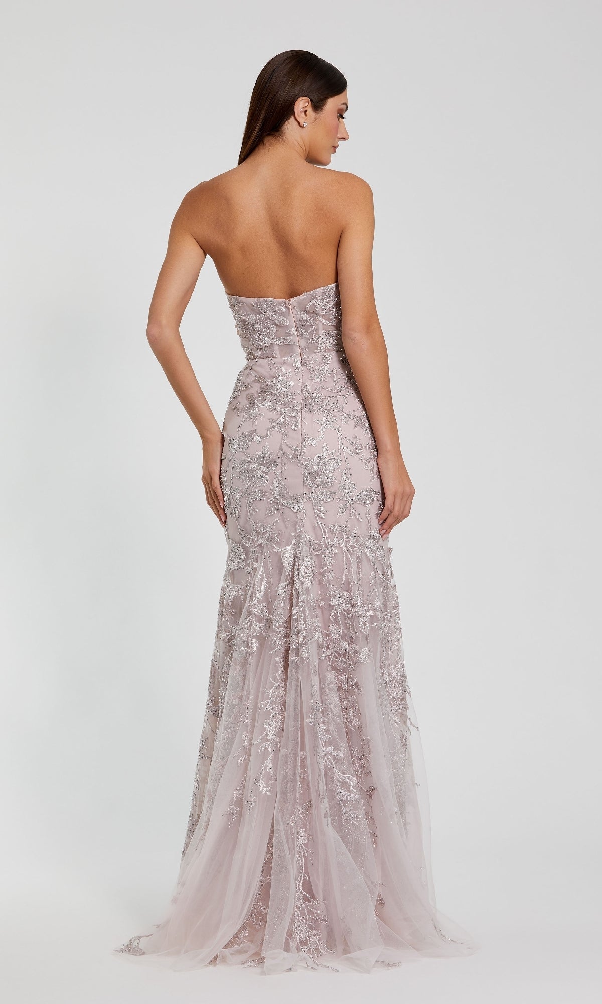 A woman is shown from the back wearing the Mac Duggal 21036 Strapless Long Floral Prom Dress in mocha pink, with delicate lace and sequin details, set against a simple light background.