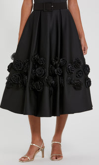 Close-up of the 3D rosette flower embellishments on the a-line skirt of a midi dress, with a white background