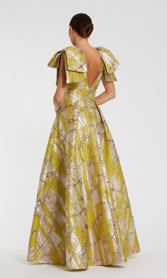 Woman wearing a yellow and white patterned evening gown with bow straps on a white background