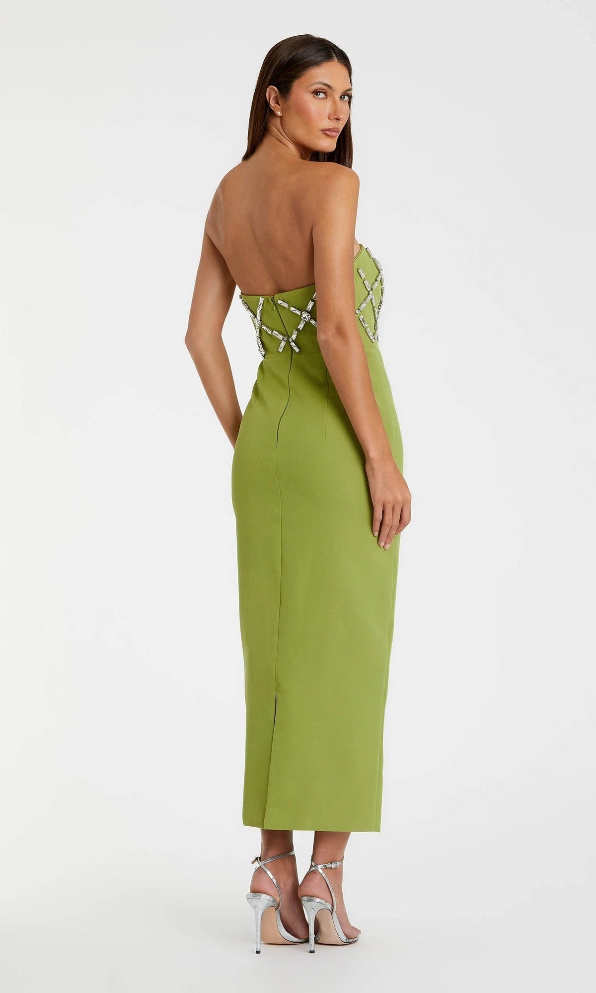 A woman in the Mac Duggal 21064 long formal dress, featuring a strapless crepe design with silver crystal embellishments, stands facing away and wears silver high-heeled sandals.