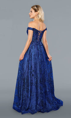 A woman faces away, wearing the Stella Couture 21064 long prom dress—a royal, off-the-shoulder gown with floral patterns and a lace-up back—set against a plain gray background.