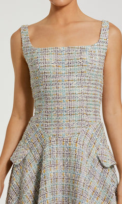 Someone wearing the Mac Duggal 21066 Midi Party Dress—a sleeveless, fitted boucle dress with a square neckline, plaid pattern, and two hip flap pockets.