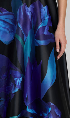 A person’s hand rests by their side, wearing the Midi Floral Semi-Formal Dress: Mac Duggal 21075, a black party dress featuring a bold blue and purple floral print.