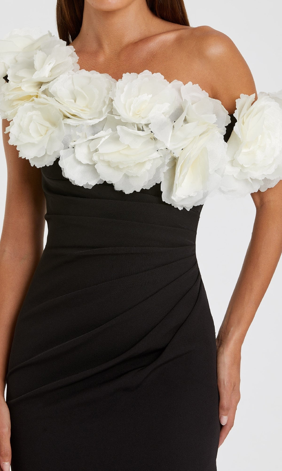 A woman wears the One-Shoulder Black Prom Gown by Mac Duggal 21079, featuring large white fabric flowers along the neckline and shoulders.