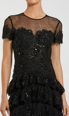 Woman wearing a black embellished evening gown standing in front of a white background