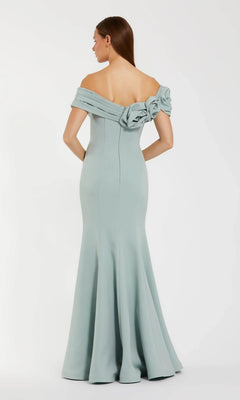 A woman models the Mac Duggal 21104 Off-Shoulder Long Formal Dress in light blue, featuring a fitted bodice and floral back detail, standing against a plain white background.