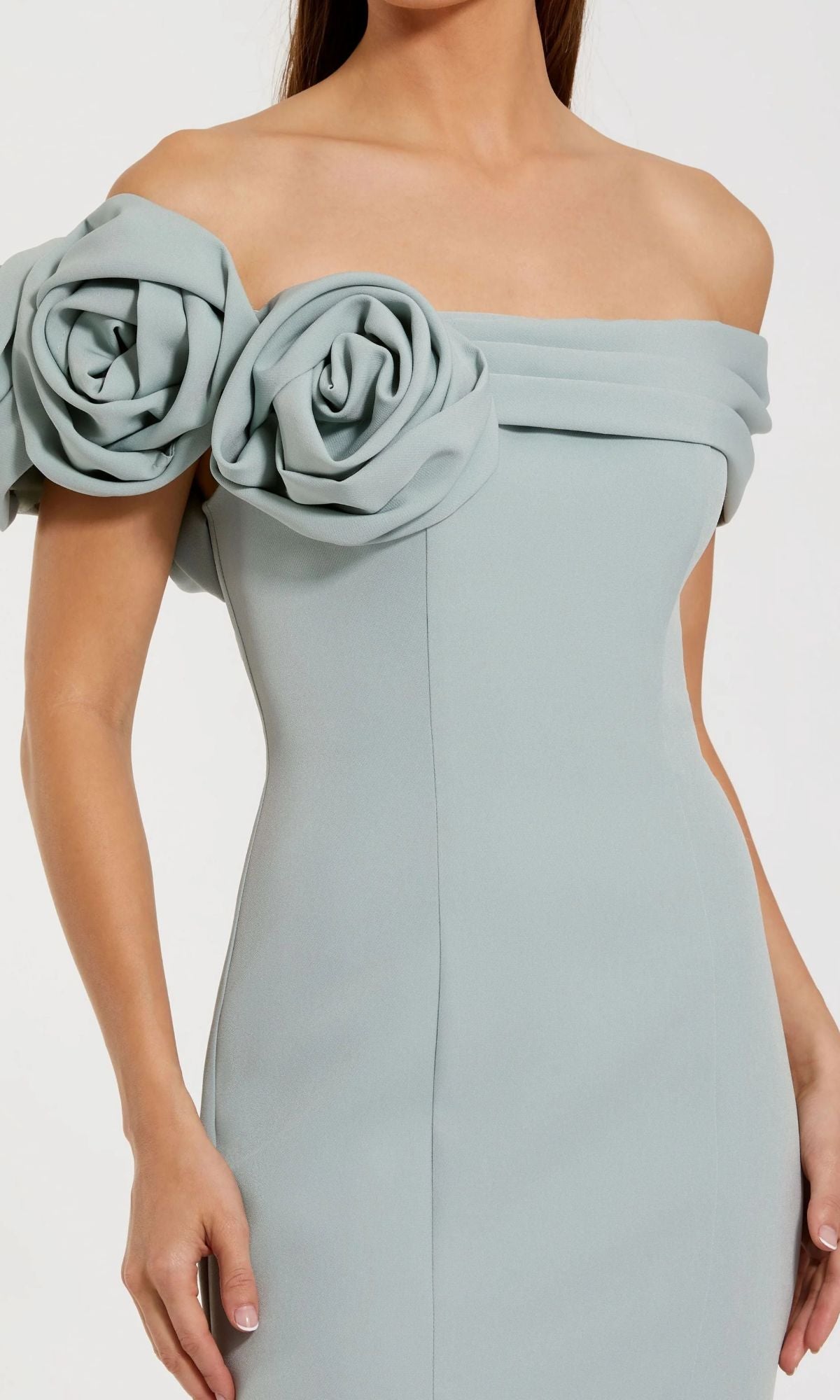 A woman wears the Mac Duggal 21104, an off-shoulder long formal dress in light blue with mermaid silhouette and large fabric rose accents on the sleeves.