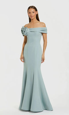 A woman in the Mac Duggal 21104 off-shoulder long formal dress, featuring a fitted bodice and large floral neckline detail, exudes elegance with its light blue, floor-length design—ideal for formal events.