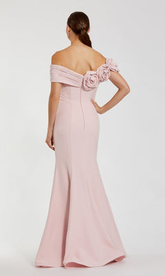 Woman in an off-shoulder Mac Duggal 21104 long formal dress in pale pink with floral detailing on the back stands against a white background, facing away from the camera.