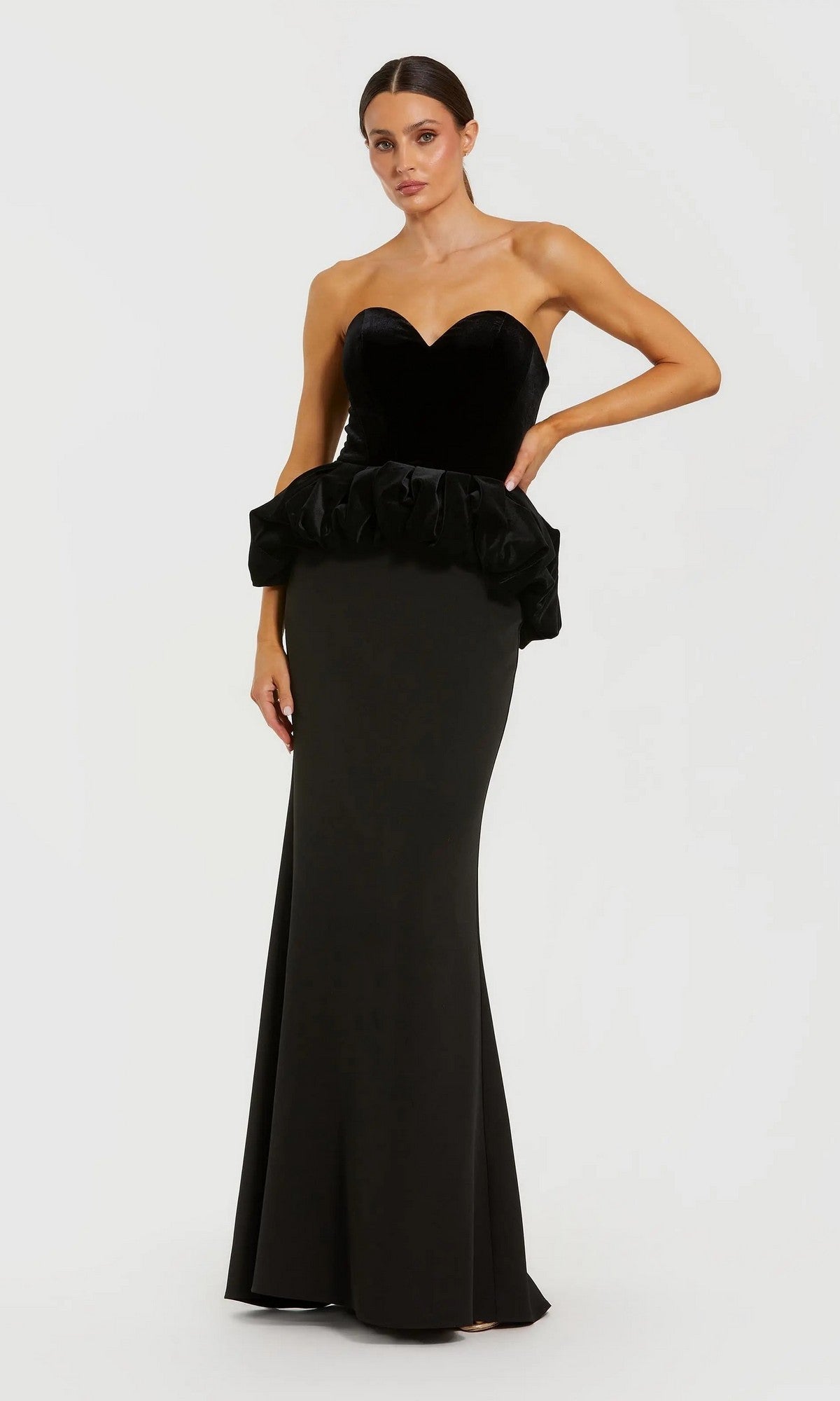 A woman stands against a white background wearing the Long Formal Dress: Mac Duggal 21145 in black—an elegant strapless evening gown featuring a velvet bodice and ruffled peplum, capturing timeless sophistication.