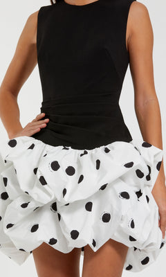 A woman wears the Mac Duggal 21150 Black and White Mini Party Dress, featuring a sleeveless black top and a white ruffled mini skirt with bold black polka dots.