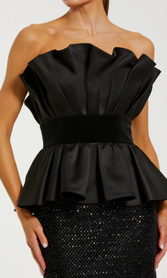 A woman wears the Mac Duggal 21174 long formal dress, featuring a strapless black ruffled bodice with a fitted waistband and a sequin column skirt for an elegant, modern look.