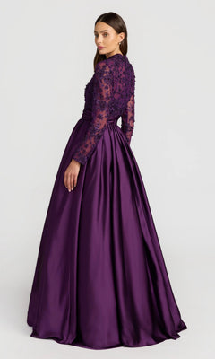 A woman in the Mac Duggal 21189 long formal dress, featuring long sleeves, a beaded-embroidered bodice, and a satin floor-length skirt, stands slightly turned from the camera against a plain background.