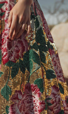 A close-up of a hand resting on the Mac Duggal 21194 long formal dress, featuring gold sequins and bold floral embroidery in red, green, and pink.