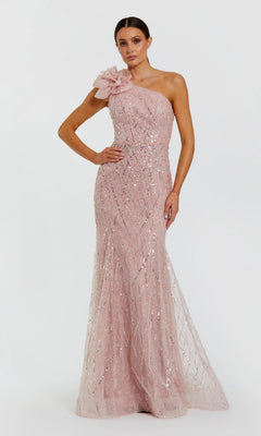 A woman wears the Mac Duggal 21199 long formal dress in rose, featuring a one-shoulder design adorned with sparkling sequins and a large floral detail on the shoulder, as she stands against a plain white background.
