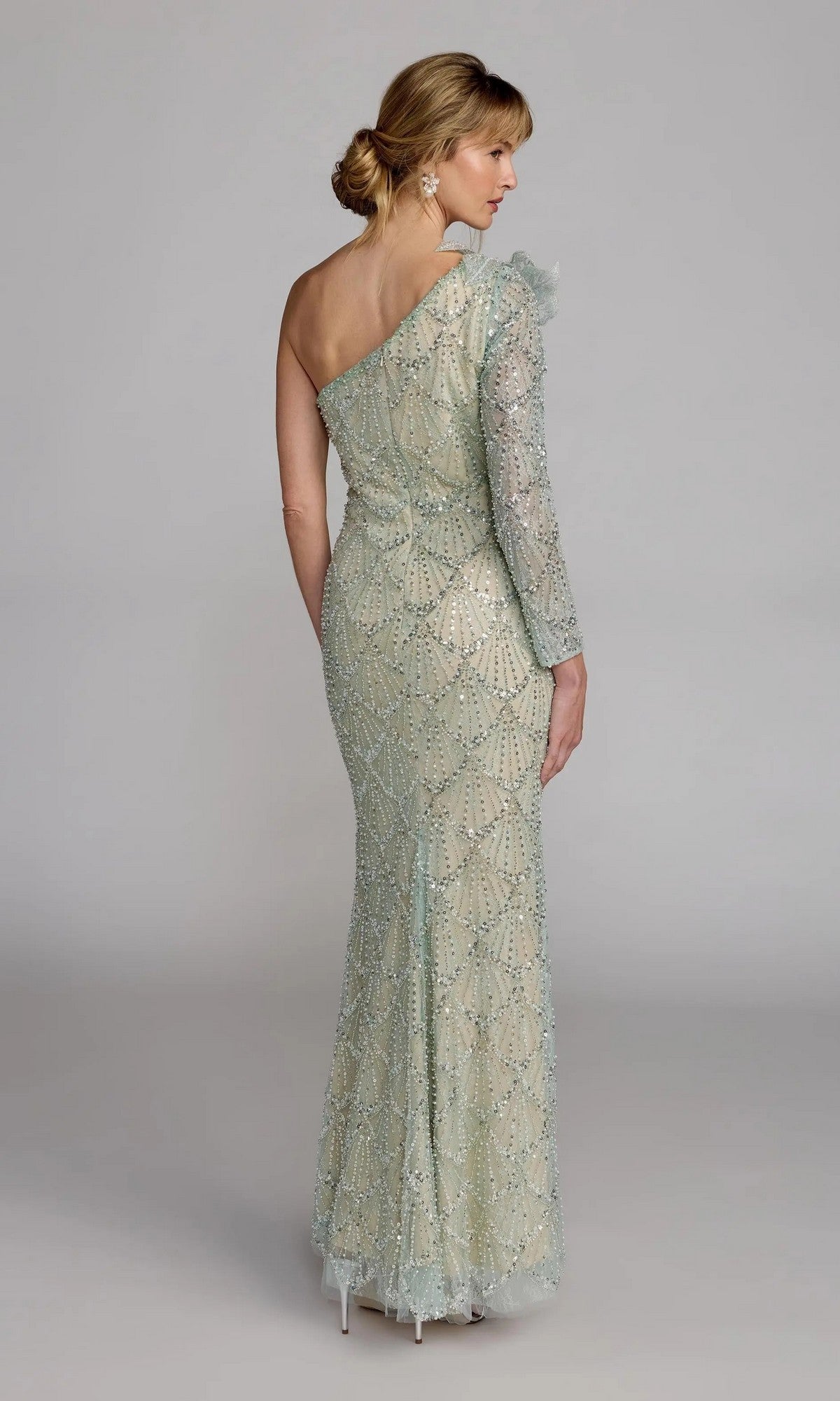 A woman faces away, wearing the Mac Duggal 21203 long formal dress—a floor-length, one-shoulder designer gown with intricate beadwork and a single long sleeve in light pastel green.