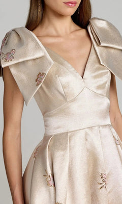Model wearing the Mac Duggal 21204 long formal dress in beige satin brocade, featuring wide pleated shoulders and delicate floral embroidery, shown from shoulders to waist against a plain background and evoking the elegance of a ballgown silhouette.