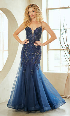 A woman stands indoors wearing the Amelia Couture 2120, a navy blue long mermaid prom dress with thin straps, embroidered lace floral details, and a tulle mermaid skirt.