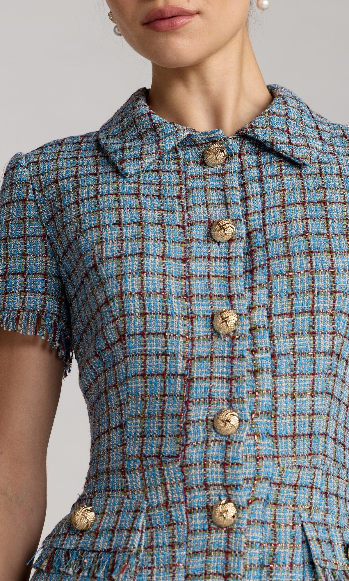 Close-up of a woman wearing the Mac Duggal 21221 Short Boucle Day Dress, featuring a blue plaid tweed fabric, gold button details, short sleeves, and a collared neckline.