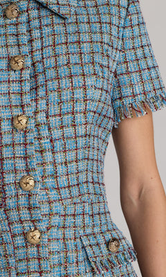Close-up of a person wearing a blue plaid tweed short-sleeve jacket with gold button detailing and frayed sleeve edges, styled over the Mac Duggal 21221 Short Boucle Day Dress and featuring a chic collared neckline.