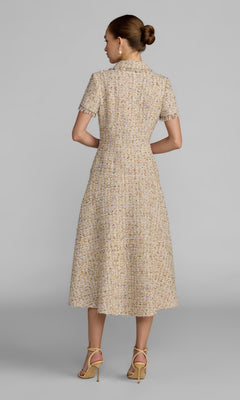 A woman stands against a plain background, facing away, dressed in the Midi Party Dress: Mac Duggal 21222—a textured, short-sleeve boucle midi dress with rhinestone buttons, an elegant A-line skirt, and paired with light-colored high-heeled sandals.