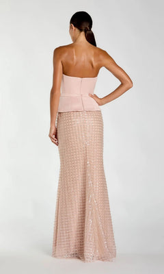 A woman stands with her back to the camera, wearing the Long Formal Dress: Mac Duggal 21227—a strapless, fitted blush pink gown featuring a peplum waist and a floor-length sequin skirt. Her hair is styled in a low ponytail.