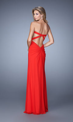 Woman wearing the La Femme Dress 21233, a floor-length red jersey net gown with crisscross straps and a strapless bodice, posing against a plain gray background.