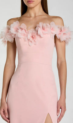 A woman wearing the Mac Duggal 21235 long formal dress in pale pink, styled with an off-shoulder sweetheart neckline accented by large fabric flower details and a thigh-high slit in luxurious crepe-jersey.