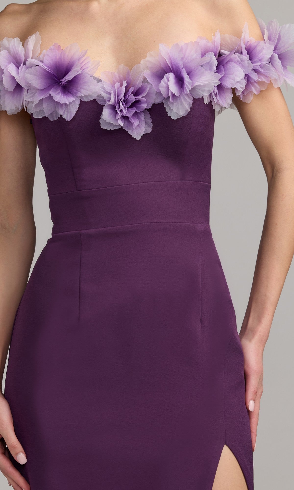 A person wearing the Mac Duggal 21235 long formal dress, which features an off-the-shoulder sweetheart neckline, a fitted waist, a thigh-high slit, and decorative lavender flowers along the neckline in purple crepe-jersey.