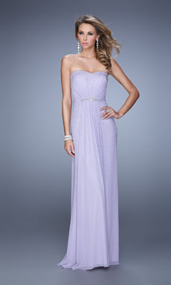 A woman wears the La Femme Embellished-Jersey Prom Dress 21237, a strapless lavender floor-length gown with a fitted bodice and beaded details, paired with jewelry, standing against a plain gray background.