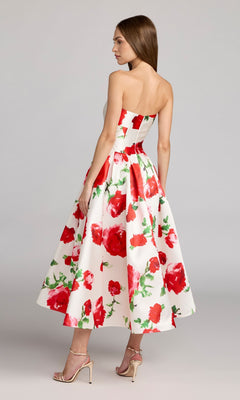 A woman stands sideways against a plain background, wearing the Mac Duggal 21238 tea-length party dress featuring a strapless design and delicate rose print, paired with beige high-heeled sandals.