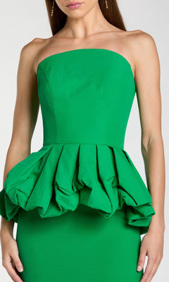 A woman showcases a chic Mac Duggal 21243 long formal dress, featuring a green strapless design with a structured, ruffled peplum at the waist.