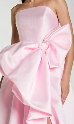 A woman wears the Long Formal Dress: Mac Duggal 21245, a strapless ballgown in elegant pastel pink, distinguished by a large, dramatic bow on the front.