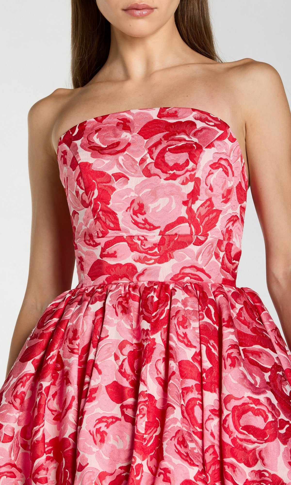 A woman wearing the Long Formal Dress: Mac Duggal 21254, a strapless pink floral ballgown with a fitted bodice and pleated skirt, beautifully adorned with vibrant red and pink blooms.