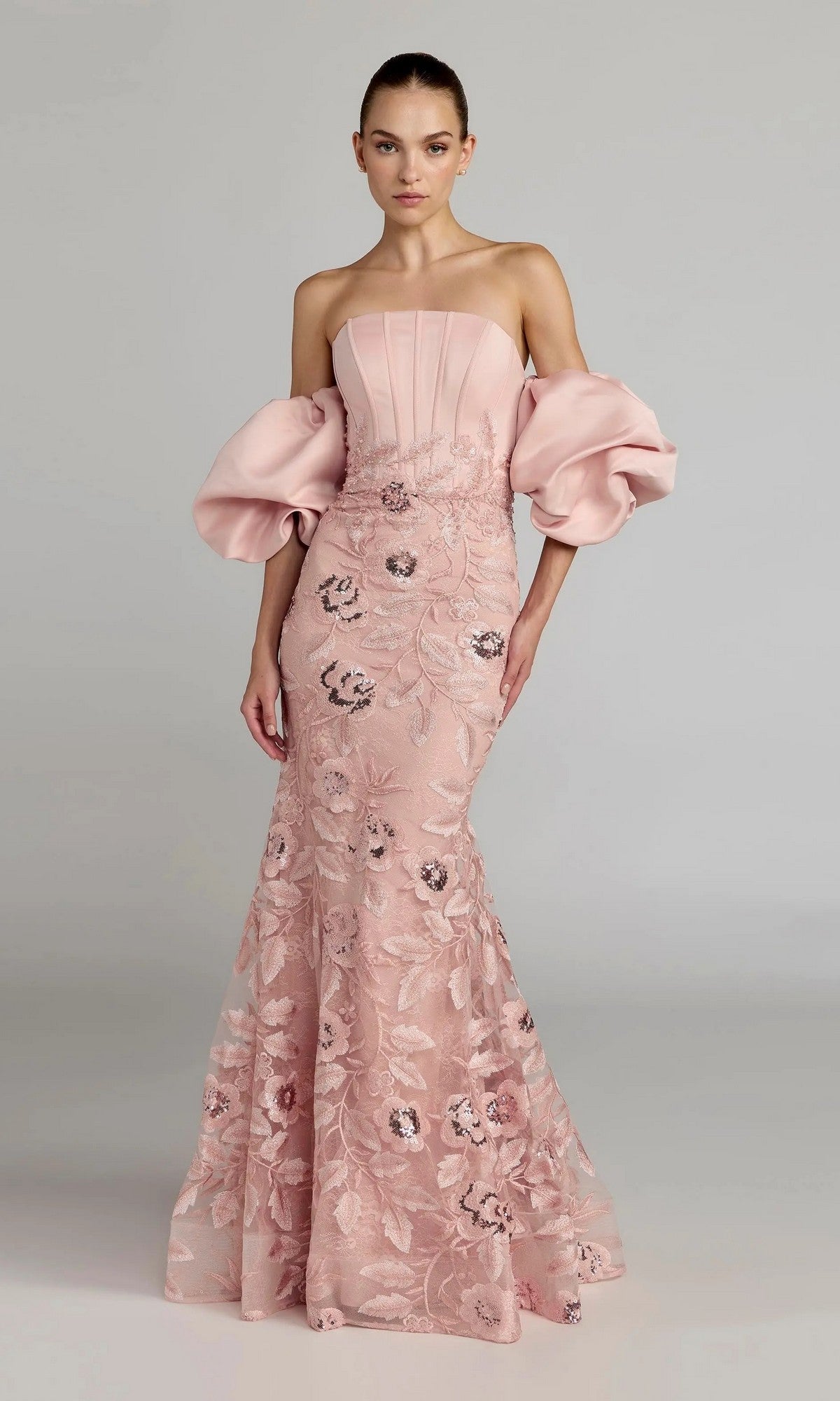 A woman wearing the Mac Duggal 21260 long formal dress in rose—a strapless satin trumpet gown featuring voluminous off-the-shoulder puff sleeves and delicate floral lace embroidery—stands against a plain background.