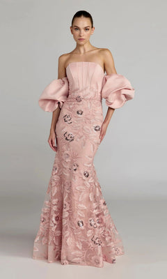 A woman wearing the Mac Duggal 21260 long formal dress in rose—a strapless satin trumpet gown featuring voluminous off-the-shoulder puff sleeves and delicate floral lace embroidery—stands against a plain background.