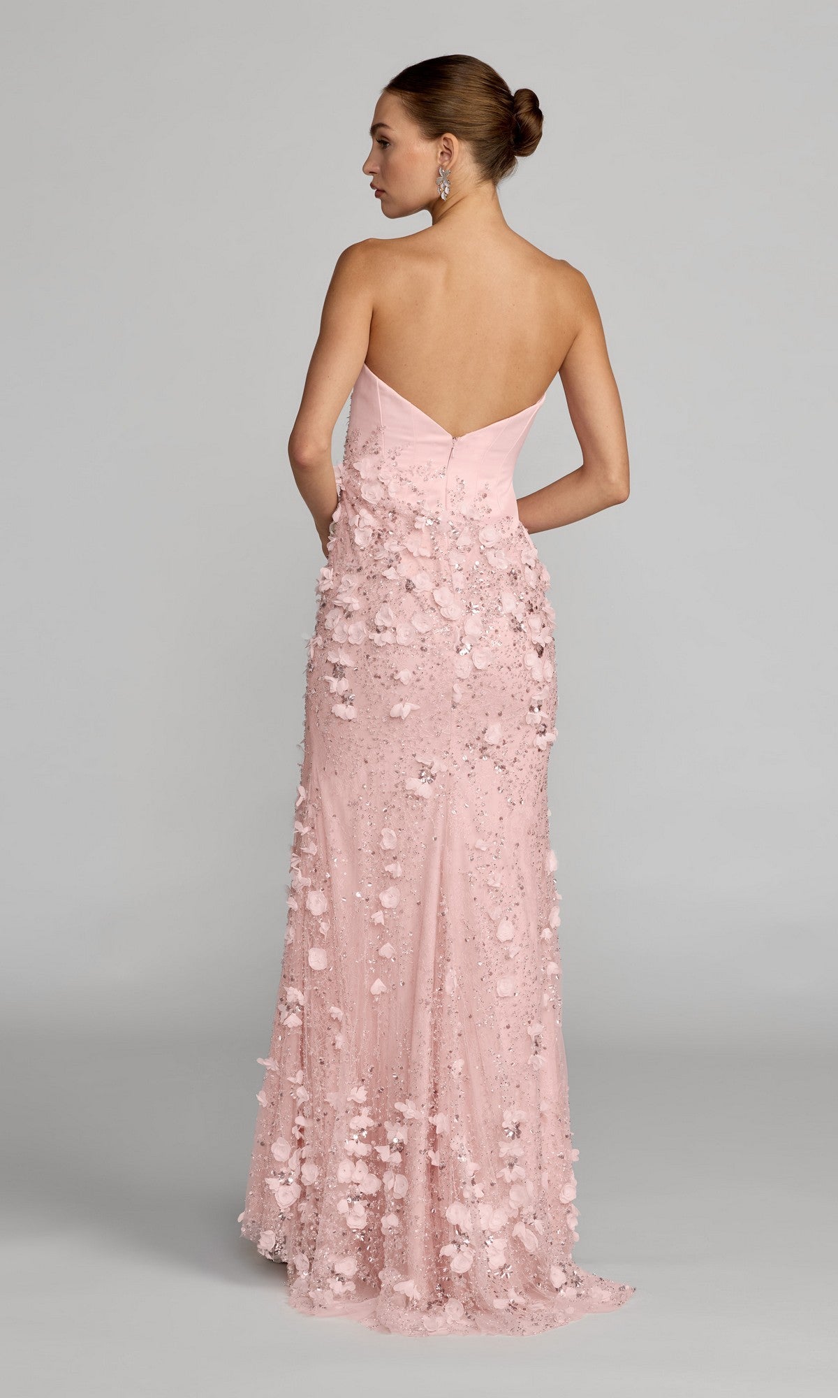 A woman wearing the Mac Duggal 21261 long formal dress, featuring a strapless sweetheart neckline and delicate 3D flower embellishments on satin, stands against a plain background with her back to the camera.