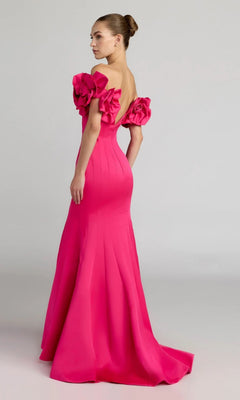 A woman stands against a plain background, looking over her shoulder in the sophisticated Mac Duggal 21263: a floor-length, hot-pink satin formal dress with off-the-shoulder ruffled sleeves—an ensemble that exudes elegance.